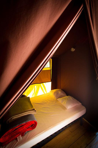 Binnenkant van een safaritent met bed, kussens en dekens bij Bivouac nature in Frankrijk.