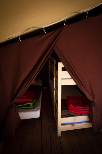 Innenraum eines Safari-Zeltes im Bivouac nature in Frankreich mit Holzfußboden, Betten und Decken.