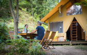 Famiglia che cena all'aperto davanti a una tenda safari Cabane al Bivouac nature, Francia, immersa nel verde.