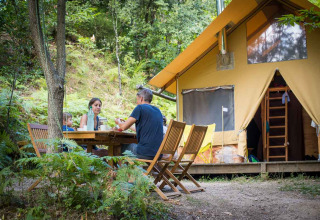 Familie beim Essen vor einem Safarizelt namens Cabane im Bivouac nature, Frankreich, umgeben von Natur.