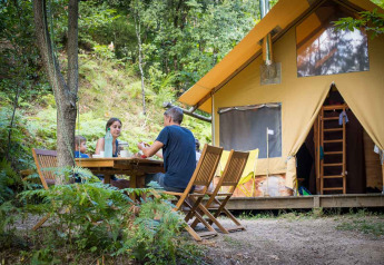 Famiglia che cena all'aperto davanti a una tenda safari Cabane al Bivouac nature, Francia, immersa nel verde.
