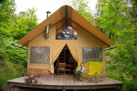 Donna seduta su sedie gialle davanti alla tenda safari Cabane, immersa nella natura verde della foresta.