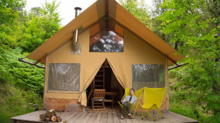 Femme assise devant la tente safari Cabane en pleine forêt, avec chaises jaunes et bois sur la terrasse.