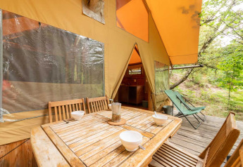 Table et chaises en bois devant la tente safari Cabane à Bivouac nature, en France.