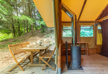 Tienda safari Cabane en Bivouac nature, Francia, con comedor exterior y estufa de leña en el interior.