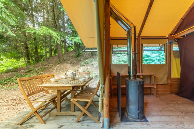 Tenda safari Cabane al Bivouac nature in Francia con tavolo da pranzo esterno e stufa a legna interna.