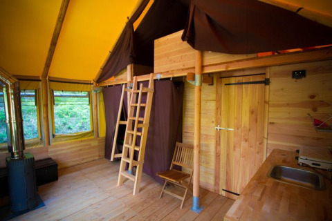 Interieur van safari tent Cabane bij Bivouac nature in Frankrijk, met houten afwerking en slaapzolder.