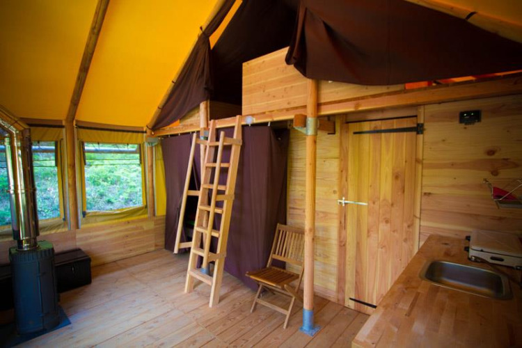 Interno della tenda safari Cabane al Bivouac nature in Francia, dotata di legno e letto soppalcato.