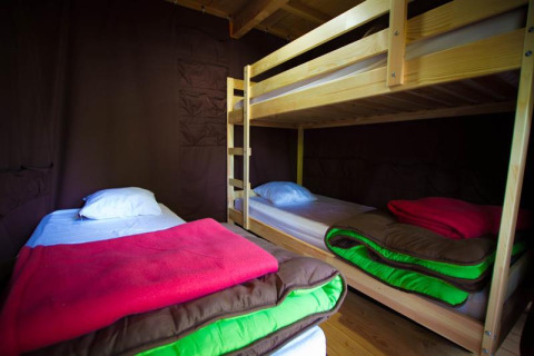 Vue intérieure de la tente safari Cabane au Bivouac Nature en France avec lits simples et lits superposés.