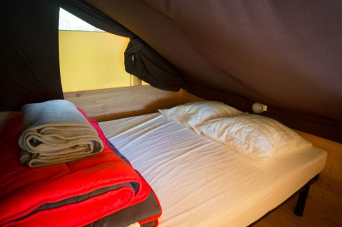 Indretning i safari-teltet Cabane ved Bivouac nature, Frankrig, med seng, dyne og tæpper.