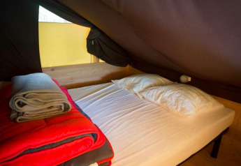 Intérieur de la tente safari Cabane à Bivouac nature en France avec lit, oreillers et couvertures.