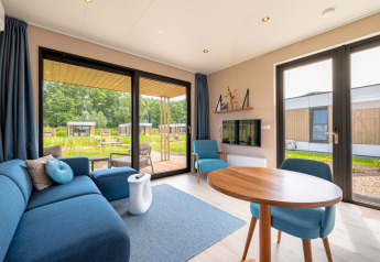 Lichte woonkamer in Water lodge 2 bij Hofparken Wiltershaar met blauwe bank, eettafel en tuinzicht.