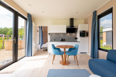 Lys stue med køkken, spisebord og blå stole, udsigt til haven fra Water lodge 2 + hot tub i Holland.