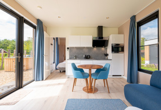 Lys stue med køkken, spisebord og blå stole, udsigt til haven fra Water lodge 2 + hot tub i Holland.
