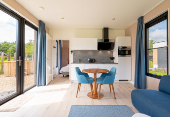 Lys stue med køkken, spisebord og blå stole, udsigt til haven fra Water lodge 2 + hot tub i Holland.