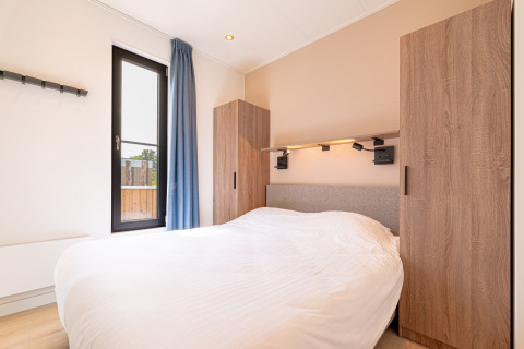 Chambre moderne à Water lodge 2 + hot tub, Hofparken Wiltershaar, Pays-Bas, avec lit et armoires en bois.