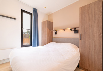 Moderne slaapkamer met bed en houten kasten in Water lodge 2 + hot tub bij Hofparken Wiltershaar, Nederland.