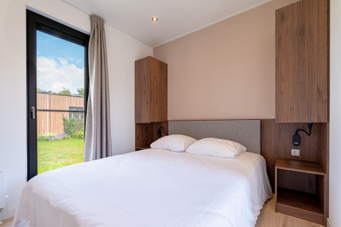 Chambre lumineuse dans une lodge avec lit double, placards en bois et vue sur le jardin.