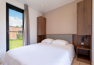 Bright lodge bedroom with double bed, wooden cabinets, window, and garden view outside.