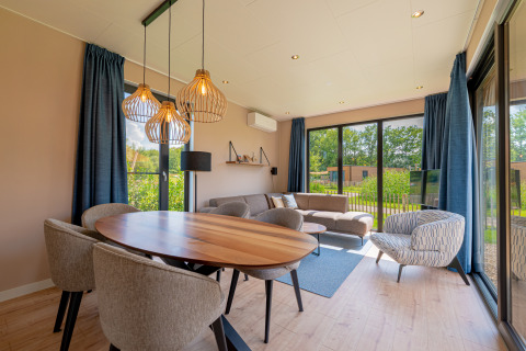 Moderne lodge woonkamer met grote ramen, eettafel, bank en uitzicht op de tuin bij Hofparken Wiltershaar.