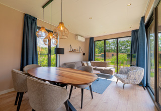 Moderne lodge woonkamer met grote ramen, eettafel, bank en uitzicht op de tuin bij Hofparken Wiltershaar.