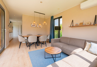 Gezellig interieur van Parklodge 6 met ruime eethoek, zithoek, houten vloer en grote ramen.