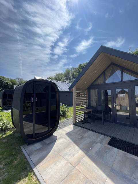 Udendørs foto af Berg Lodge med en moderne saunaenhed og solrigt vejr under en blå himmel.