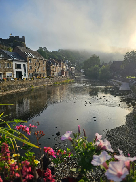 Uitzicht vanaf een glamping over een rustige rivier, kleurrijke bloemen en schilderachtige huizen aan de oever.