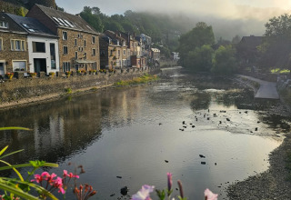 Vista da un alloggio glamping su un fiume tranquillo, fiori colorati e case pittoresche sull’argine.