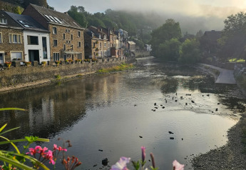 Udsigt fra glamping over en stille flod, farverige blomster i forgrunden og maleriske huse ved vandet.