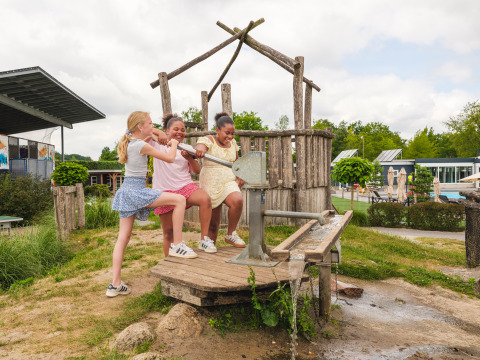 Drie kinderen spelen bij een waterpomp op de speelplaats in Vakantiepark Ackersate, Gelderland, Nederland.