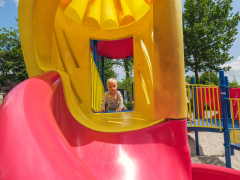 Bambino piccolo che gioca su uno scivolo colorato nel parco giochi di Holiday park Ackersate, Gelderland, Paesi Bassi.