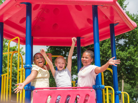 Tres niños felices juegan en un colorido parque infantil bajo un techo rosa en Holiday park Ackersate, Gelderland.