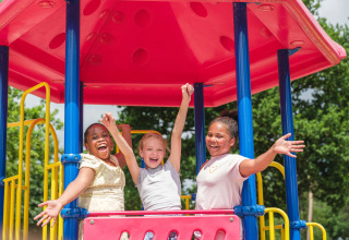 Three joyful children play on a colorful playground under a pink roof at Holiday park Ackersate, Gelderland.