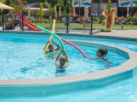 Children playing with pool noodles in the swimming pool at Holiday park Ackersate, Gelderland, Netherlands.