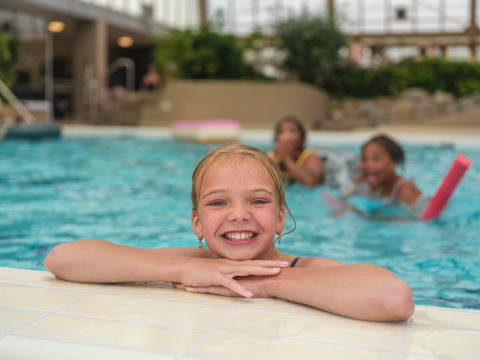 Bambina sorridente sul bordo di una piscina coperta all’Holiday park Ackersate, Gelderland, Paesi Bassi, con amici.