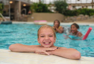 Bambina sorridente sul bordo di una piscina coperta all’Holiday park Ackersate, Gelderland, Paesi Bassi, con amici.