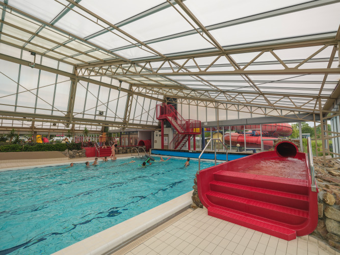 Hallenbad mit roter Wasserrutsche und schwimmenden Gästen im Holiday Park Ackersate in Gelderland, Niederlande.