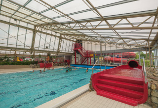 Overdekt zwembad met rode waterglijbaan en zwemmers in Holiday park Ackersate in Gelderland, Nederland.