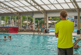 Kinder springen in ein überdachtes Schwimmbad im Holiday Park Ackersate, beaufsichtigt von einem Bademeister.