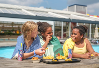 Trois enfants mangent des frites et boivent un soda près de la piscine au parc de vacances Ackersate, Pays-Bas.