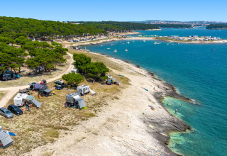 Campeggio costiero vicino a Premantura, Istria, Croazia, con tende, camper, pini e mare blu brillante.