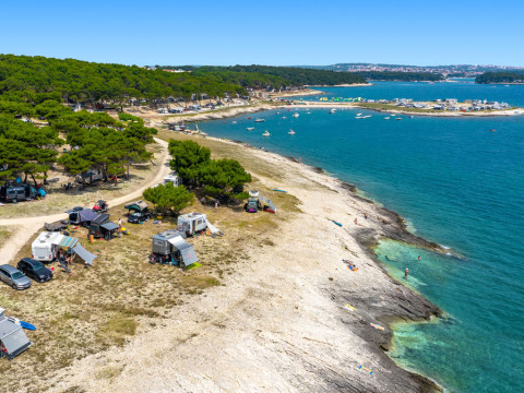 Campeggio costiero vicino a Premantura, Istria, Croazia, con tende, camper, pini e mare blu brillante.