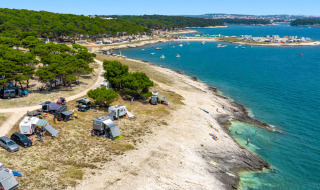 Campingplads ved kysten nær Premantura, Istrien, Kroatien med telte, campingvogne og smukt blåt hav.