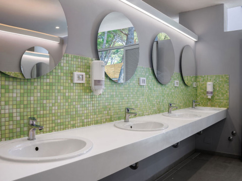 Bagno comune moderno con specchi rotondi, piastrelle verdi e diversi lavabi in un villaggio vacanze in Croazia.