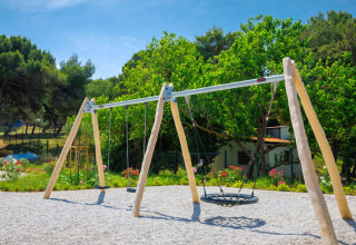 Playground swings under trees at Camping Arena Stupice holiday park in Istria, Croatia on a sunny day.
