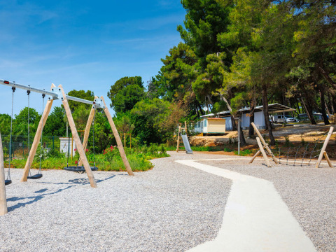 Aire de jeux avec balançoires, toboggan et filet à grimper au Camping Arena Stupice en Istrie, Croatie, bordée d’arbres.