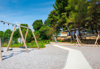 Area giochi con altalene, scivolo e rete da arrampicata al Camping Arena Stupice in Istria, Croazia, circondata dagli alberi.
