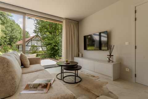 Moderne woonkamer in Woodz Lodges met zetel, salontafels, tv en grote ramen met tuinzicht.