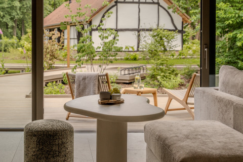 Zicht vanuit de leefruimte van Suite at Woodz Lodges, België, op terras en vakwerkhuis midden in het groen.